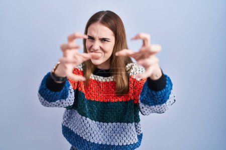 Photo for Young hispanic girl standing over blue background shouting frustrated with rage, hands trying to strangle, yelling mad - Royalty Free Image