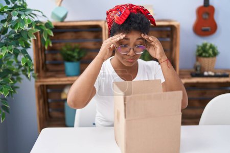 Foto de Mujer afroamericana desempacando caja de cartón con expresión infeliz en casa - Imagen libre de derechos