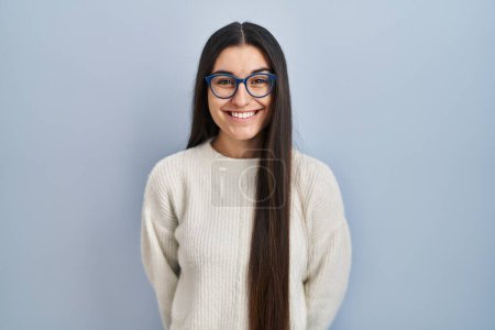 Téléchargez les photos : Jeune femme hispanique portant un pull décontracté sur fond bleu avec un sourire heureux et cool sur le visage. chanceux. - en image libre de droit
