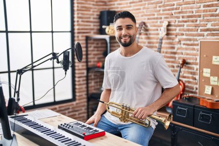 Foto de Joven músico árabe sonriendo confiado sosteniendo trompeta en el estudio de música - Imagen libre de derechos