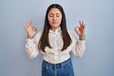 Téléchargez les photos : Jeune femme latine debout sur fond bleu détendue et souriante avec les yeux fermés faisant geste de méditation avec les doigts. concept de yoga. - en image libre de droit