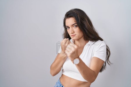 Photo for Young teenager girl standing over white background ready to fight with fist defense gesture, angry and upset face, afraid of problem - Royalty Free Image