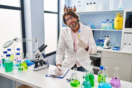 Téléchargez les photos : Homme d'âge moyen scientifique tenant un tube à essai écrivant sur un document au laboratoire - en image libre de droit
