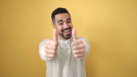 Foto de Joven hispano sonriendo confiado haciendo ok signo con pulgares arriba sobre aislado amarillo fondo - Imagen libre de derechos