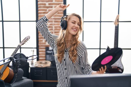 Téléchargez les photos : Jeune femme blonde dj tenant un disque vinyle et dansant au studio de musique - en image libre de droit