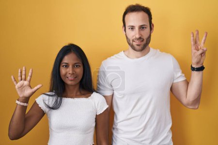 Téléchargez les photos : Couple interracial debout sur fond jaune montrant et pointant vers le haut avec les doigts numéro huit tout en souriant confiant et heureux. - en image libre de droit