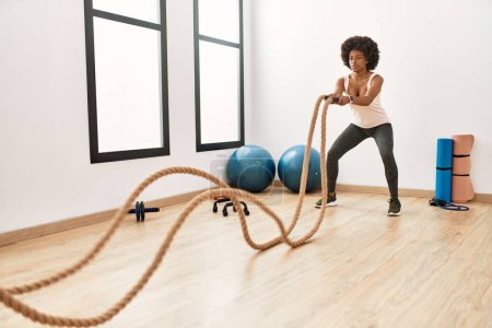 Photo for Young african american woman training with battle rope at sport center - Royalty Free Image