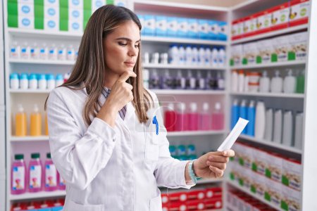 Foto de Joven bella mujer hispana farmacéutica leyendo prescripción en farmacia - Imagen libre de derechos