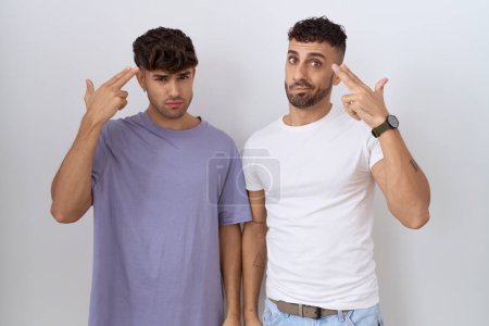 Foto de Homosexual pareja gay de pie sobre blanco fondo disparo y matándose apuntando la mano y los dedos a la cabeza como arma, gesto suicida. - Imagen libre de derechos