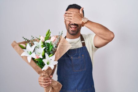 Photo for Hispanic man with beard working as florist smiling and laughing with hand on face covering eyes for surprise. blind concept. - Royalty Free Image