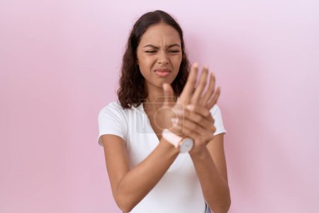 Téléchargez les photos : Jeune femme hispanique portant un t-shirt blanc occasionnel souffrant de douleur aux mains et aux doigts, inflammation de l'arthrite - en image libre de droit