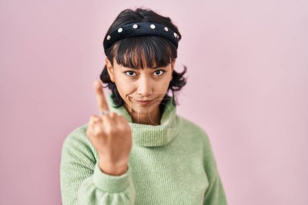 Foto de Young beautiful woman standing over pink background showing middle finger, impolite and rude fuck off expression - Imagen libre de derechos