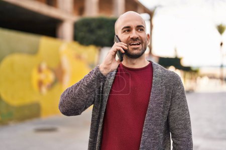 Téléchargez les photos : Jeune homme souriant confiant parler sur le smartphone à la rue - en image libre de droit