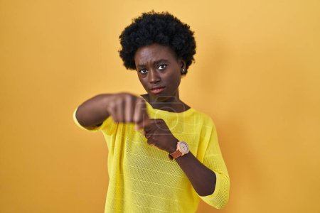 Téléchargez les photos : Jeune femme africaine debout au-dessus du poing jaune studio de coups de poing pour se battre, attaque agressive et en colère, menace et violence - en image libre de droit