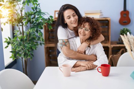 Foto de Two women mother and daughter drinking coffee hugging each other at home - Imagen libre de derechos