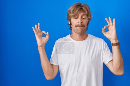 Photo for Middle age man standing over blue background relaxed and smiling with eyes closed doing meditation gesture with fingers. yoga concept. - Royalty Free Image