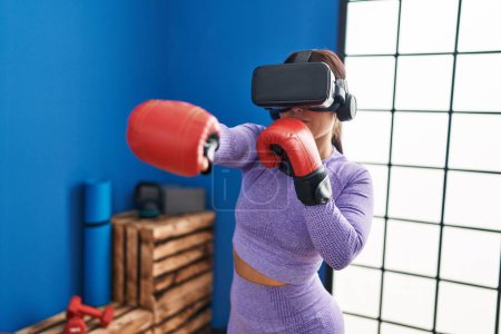 Téléchargez les photos : Jeune belle femme hispanique utilisant des lunettes de réalité virtuelle boxe au centre sportif - en image libre de droit