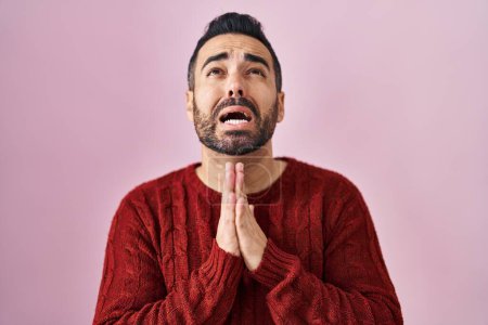 Photo for Young hispanic man with beard wearing casual sweater over pink background begging and praying with hands together with hope expression on face very emotional and worried. begging. - Royalty Free Image