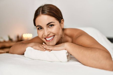 Téléchargez les photos : Jeune belle femme hispanique souriant confiant couché sur la table de massage au salon de beauté - en image libre de droit