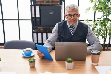 Téléchargez les photos : Homme d'affaires aux cheveux gris d'âge moyen utilisant un ordinateur portable et un pavé tactile au bureau - en image libre de droit