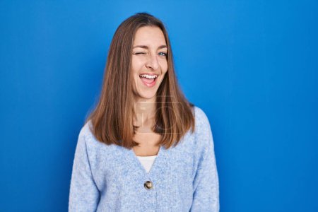Photo for Young woman standing over blue background winking looking at the camera with sexy expression, cheerful and happy face. - Royalty Free Image