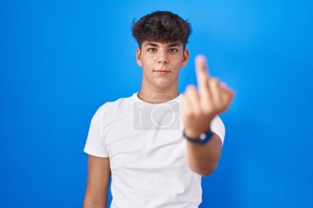 Foto de Hispanic teenager standing over blue background showing middle finger, impolite and rude fuck off expression - Imagen libre de derechos