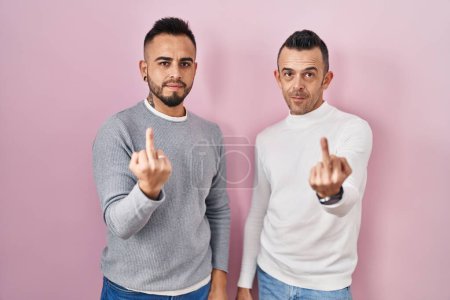 Foto de Homosexual couple standing over pink background showing middle finger, impolite and rude fuck off expression - Imagen libre de derechos