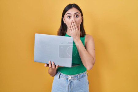 Photo for Hispanic girl working using computer laptop covering mouth with hand, shocked and afraid for mistake. surprised expression - Royalty Free Image