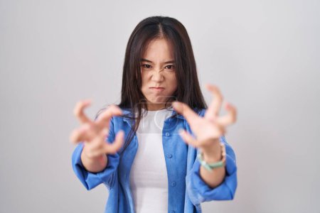 Photo for Young chinese woman standing over white background shouting frustrated with rage, hands trying to strangle, yelling mad - Royalty Free Image