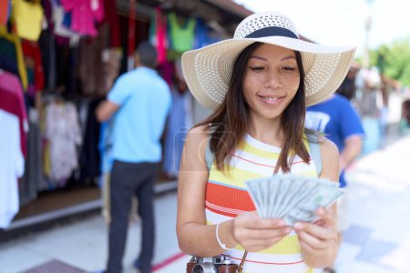 Foto de Young asian woman tourist smiling confident counting dollars at street market - Imagen libre de derechos