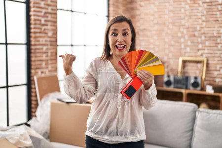 Photo for Middle age hispanic woman choosing color of new house wall pointing thumb up to the side smiling happy with open mouth - Royalty Free Image