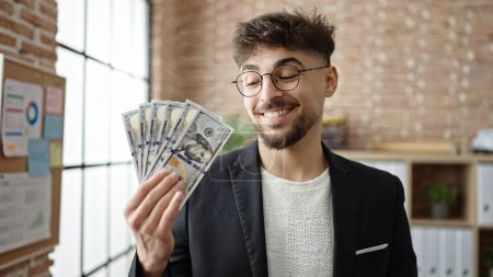 Foto de Joven árabe hombre de negocios trabajador sonriendo confiado sosteniendo dólares en la oficina - Imagen libre de derechos