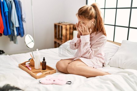 Foto de Mujer joven caucásica aplicando tratamiento de loción de piel sentada en la cama en el dormitorio - Imagen libre de derechos