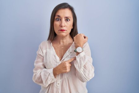 Téléchargez les photos : Moyen Age femme hispanique debout sur fond bleu pressé pointant vers regarder le temps, impatience, regardant la caméra avec une expression détendue - en image libre de droit