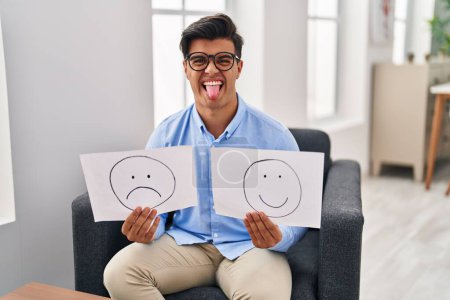 Téléchargez les photos : Homme hispanique travaillant sur la dépression tenant triste à papier émotionnel heureux coller la langue heureux avec une expression drôle. - en image libre de droit