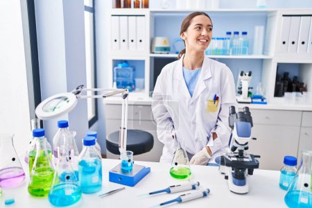 Téléchargez les photos : Jeune femme brune travaillant au laboratoire scientifique regardant de côté avec le sourire sur le visage, expression naturelle. riant confiant. - en image libre de droit