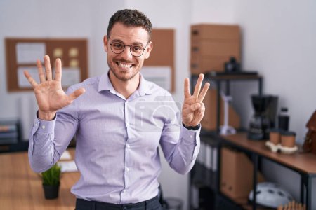 Téléchargez les photos : Jeune homme hispanique au bureau montrant et pointant vers le haut avec les doigts numéro huit tout en souriant confiant et heureux. - en image libre de droit
