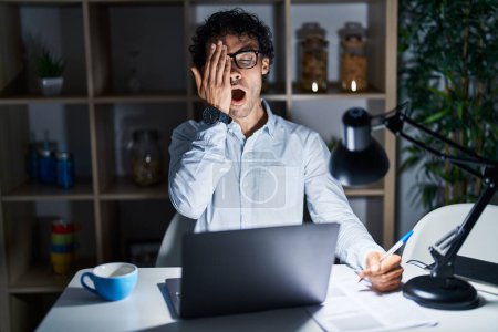 Photo for Hispanic man working at the office at night yawning tired covering half face, eye and mouth with hand. face hurts in pain. - Royalty Free Image