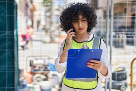Téléchargez les photos : Young middle east woman architect talking on smartphone reading document at street - en image libre de droit