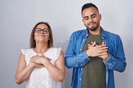 Téléchargez les photos : Mère hispanique et son fils debout ensemble souriant avec les mains sur la poitrine avec les yeux fermés et geste reconnaissant sur le visage. concept de santé. - en image libre de droit