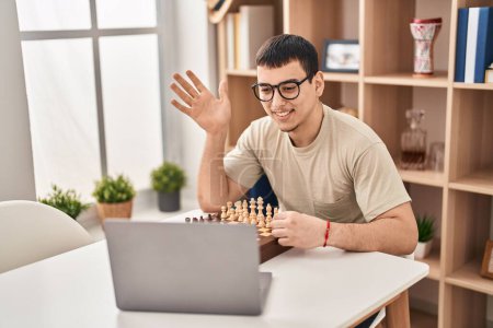 Téléchargez les photos : Jeune homme arabe jouant aux échecs en ligne célébrant la réalisation avec un sourire heureux et l'expression gagnante avec la main levée - en image libre de droit