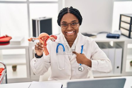 Téléchargez les photos : Médecin afro-américain femme tenant le modèle anatomique de l'organe génital féminin pointant du doigt un sourire heureux et fier - en image libre de droit