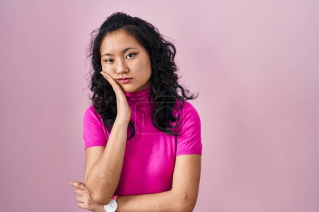 Foto de Young asian woman standing over pink background thinking looking tired and bored with depression problems with crossed arms. - Imagen libre de derechos