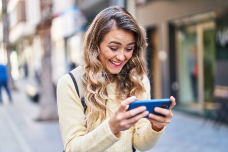 Téléchargez les photos : Jeune femme touriste souriant confiant regarder la vidéo sur smartphone à la rue - en image libre de droit