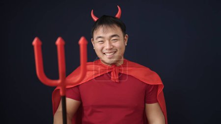 Téléchargez les photos : Jeune homme chinois portant costume diable tenant trident sur fond noir isolé - en image libre de droit