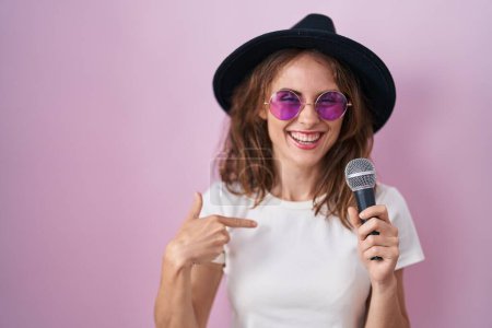 Photo for Beautiful brunette woman singing song using microphone pointing finger to one self smiling happy and proud - Royalty Free Image