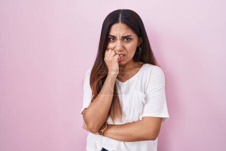 Foto de Mujer árabe joven de pie sobre fondo rosa mirando estresada y nerviosa con las manos en la boca mordiendo las uñas. problema de ansiedad. - Imagen libre de derechos