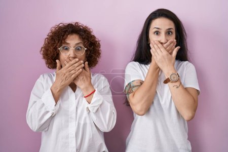 Photo for Hispanic mother and daughter wearing casual white t shirt over pink background shocked covering mouth with hands for mistake. secret concept. - Royalty Free Image