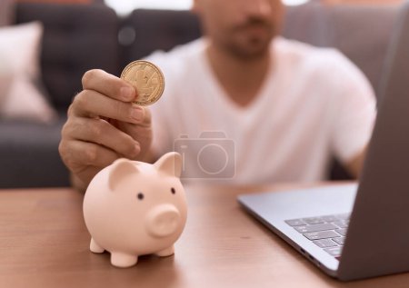 Photo for Young hispanic man inserting litecoin crypto currency on piggy bank at home - Royalty Free Image