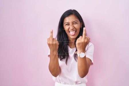 Foto de Young hispanic woman standing over pink background showing middle finger doing fuck you bad expression, provocation and rude attitude. screaming excited - Imagen libre de derechos